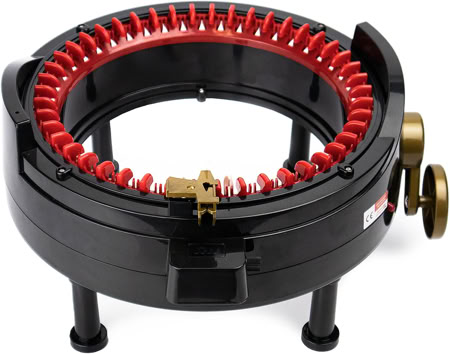 A circular knitting machine with red needles and a black base, placed on a white surface.